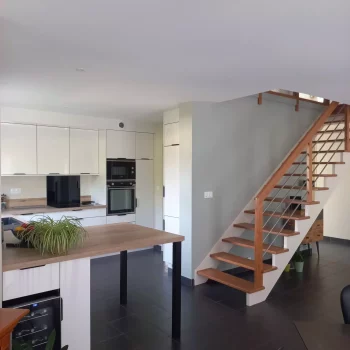 Cuisine blanche ouverte sur le séjour avec escalier en bois