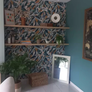 Coin détente avec papier peint feuillage coloré, étagères et mur bleu